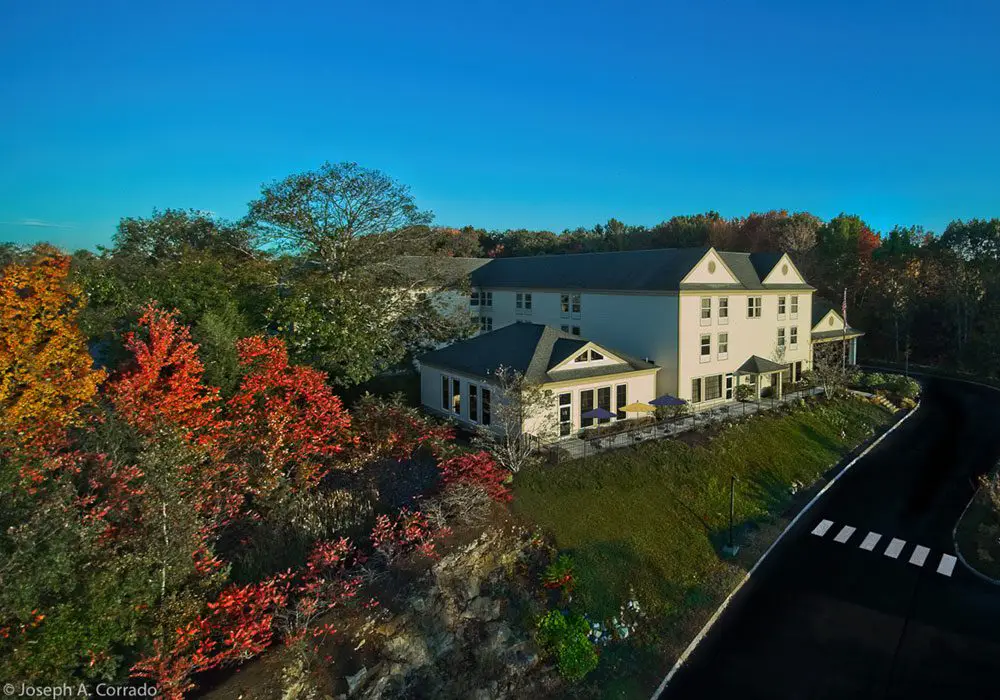 Aerial view of a large white house situated on the side of a road surrounded by trees, plants, grass